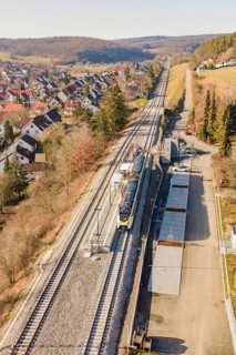 Zug travels on a railway line through a rural, densely built-up area with trees, test run on the