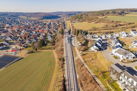 Railway tracks cross an extensive landscape with houses and fields, aerial view, test run on the