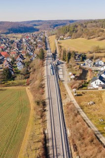 Aerial view of railroad tracks running through a rural area with houses and fields, test run on the