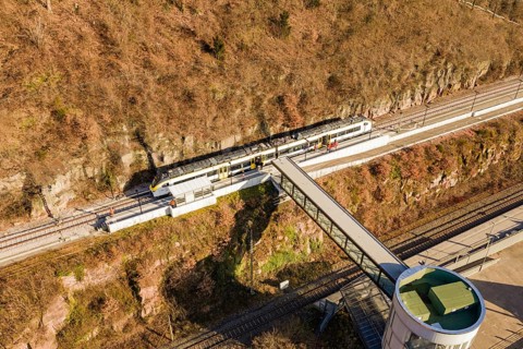 Train travels across tracks below an elevated bridge surrounded by autumn colors, test run on the