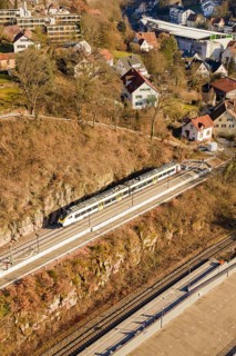 Train travels through a village on elevated tracks surrounded by hills and houses, test run on the