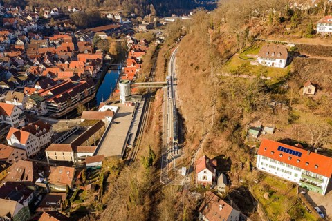 Train route through hilly village with red roofs and a river, test trip on the new Hermann-Hesse
