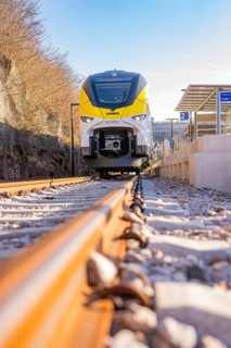 Close-up of a yellow and white train on gravel tracks at a bus stop, test run on the new
