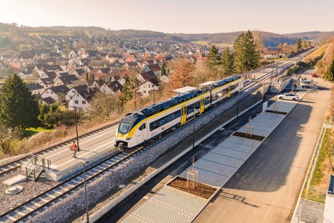 Train at a train station in a rural area surrounded by hills and houses, test ride on the new