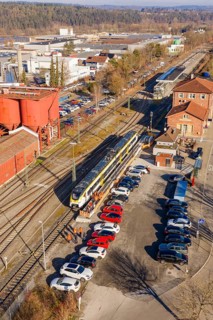 Train in a train station with adjacent parking lot and buildings in an industrial area, test run on