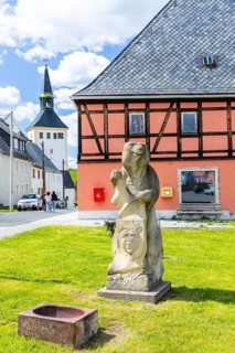 Sandstone figure bear with coat of arms on Bärenstein market square, church in the background,