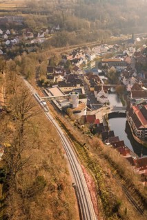 City view from the air with railway line along a wooded slope and river, test run on the new