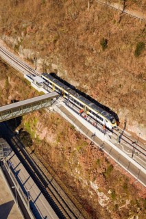 Train travels through hilly landscape over bridge surrounded by vegetation and tracks, test run on