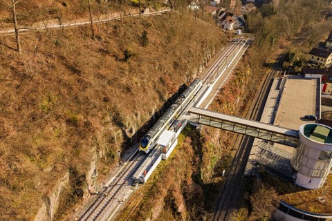 Aerial view of a train station with a train in hilly landscape and autumn colors, test run on the