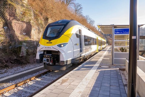 Modern train at a small train station surrounded by trees and hills, test run on the new