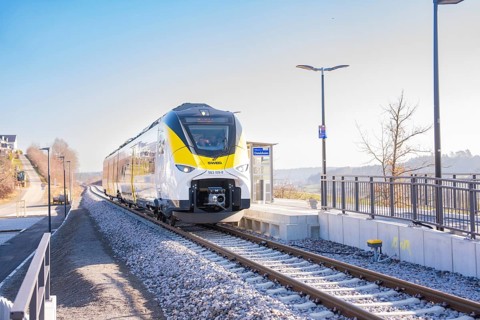 Modern train on the track in front of a small train station in sunshine, test run on the new