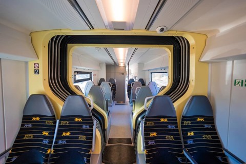 Train compartment with yellow accents and grey seats in bright surroundings, test run on the new