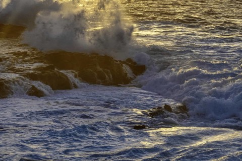 Thundering waves hit a rocky coast illuminated by soft sunlight during sunset, Playa Blanca/Yaiza
