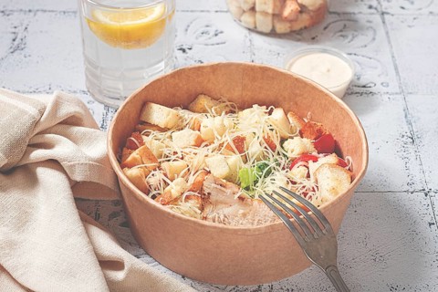 Caesar salad in a paper container, take it on the way, with sauce and croutons, on the table,
