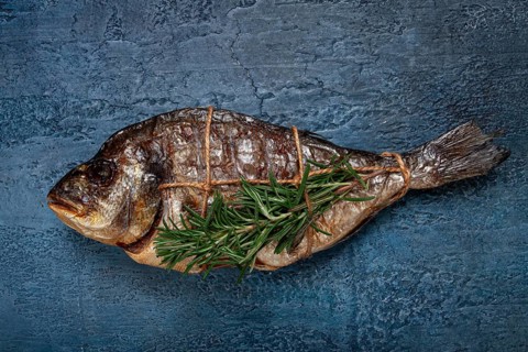 Dorado fish, hot smoked, with a sprig of rosemary, tied with a rope, on a blue background, top