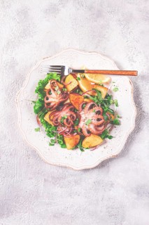 Grilled octopus with baked potatoes and fresh herbs, on a decorative light plate, homemade, no