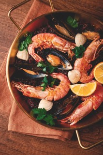 Seafood and black rice paella, in a frying pan, homemade, on a wooden table, no people