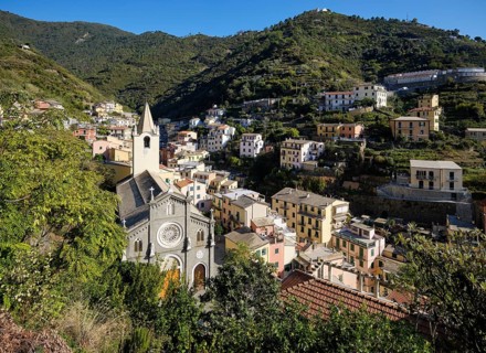 View of picturesque village of Riomaggiore with church and colorful houses in a green, hilly