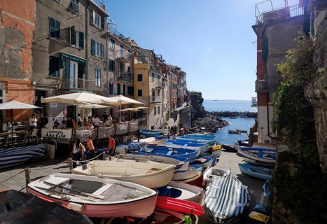 Stacked boats in front of colorful houses under a blue sky in the fishing village of Riomaggiore,