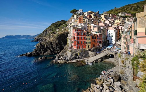 Colourful houses under blue sky, view of the fishing village of Riomaggiore, boats in the harbour,