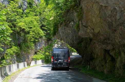 A black van drives on a narrow mountain road surrounded by lush greenery, camper, motorhome in a