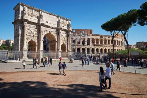 Arch of Constantine and Colosseum surrounded by tourists under blue sky and green grass, Rome,