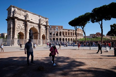 Tourists in front of the Colosseum and Arch of Constantine on a sunny day surrounded by trees,