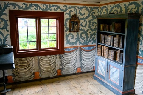 Small room with an antique bookshelf and artfully decorated walls next to a window in the
