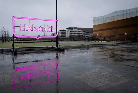 Large pink glowing Helsinki city logo, in front of Oodi Central Library and Cultural Center,