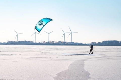 Person kiting on frozen Dümmer Lake, wind turbines in the background, Lembruch, Diepholz district,