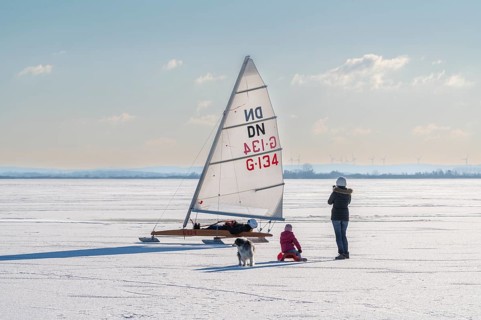 Family with dog watching sailboat on frozen Dümmer See, Lembruch, Diepholz district, Lower Saxony,