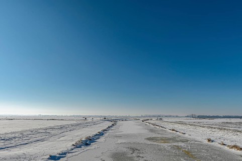 Snowy open landscape with wide sky and distant horizon under blue sky in the foreground the frozen