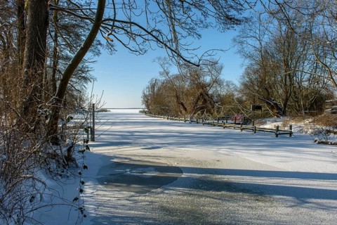 Outflow of the river Lohne from the snowy and frozen Dümmer Lake with trees in the background,
