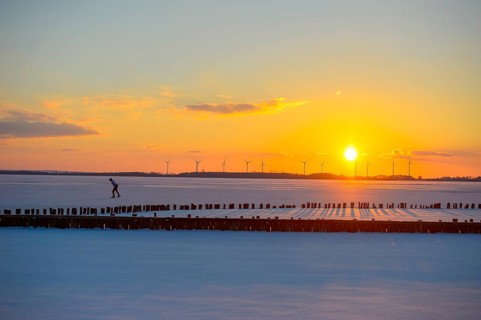 Ice skaters in front of sunset over icy landscape with wind turbines and intense colors on the