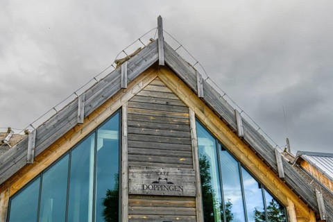 Modern building with wooden paneling and large glass windows under a cloudy sky, labelled as Café