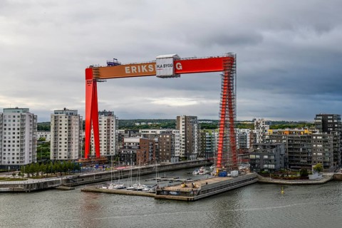 Large orange construction crane in front of modern residential buildings on the site of the former