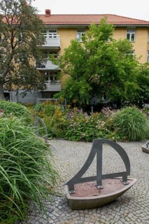 Green garden with art installations and lush plants in front of a residential building, Gothenburg,