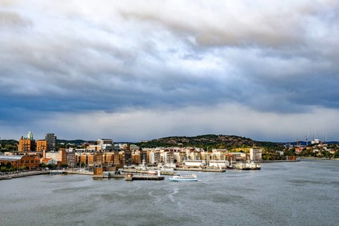 Urban landscape with waterside buildings and hills in the background under cloudy sky, Gothenburg