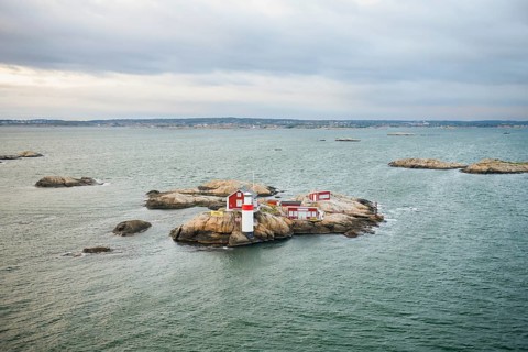 Small rocky island with lighthouse and red buildings in the calm sea, near Gothenburg, Västra