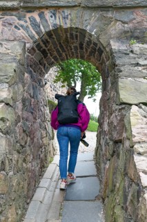 Person passes an old stone arch, a mix of history and nature in an exploration setting,