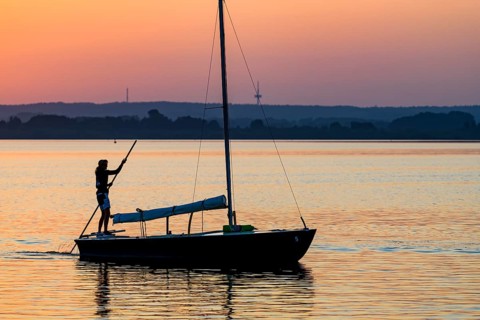 Sailing boat with person on calm Dümmer See brought into the harbor with a long stake at sunset,