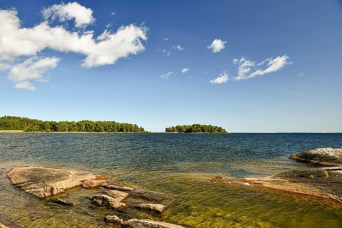 A lake with rocks in the foreground, islands on the horizon and a sky with few clouds at Lake