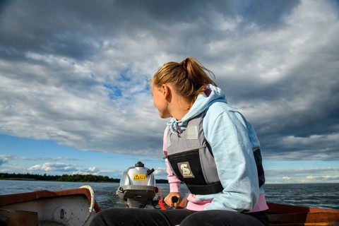 Young woman in a boat with outboard on the quiet lake Vänern, looking into the distance, the sky is