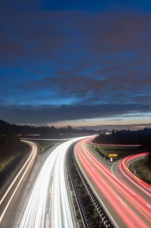 Night view of a motorway with red and white light trails against a cloudy sky, near Stuttgart,