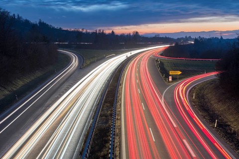 Highway view at dusk with red and white light trails, in front of an evening horizon, near