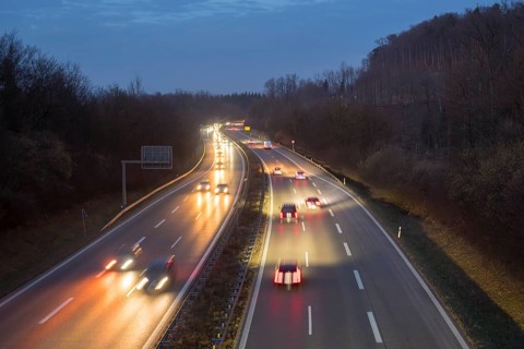 Illuminated motorway in the dark with passing cars, surrounded by hills and trees, near Stuttgart,