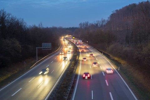 Cars move at night on an illuminated highway, surrounded by trees and darkness, near Stuttgart,