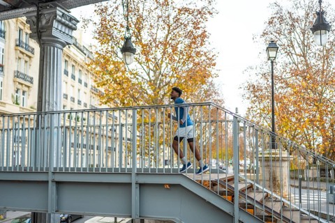 Young man in sportswear running up a metal staircase on a bridge in paris, showing active city