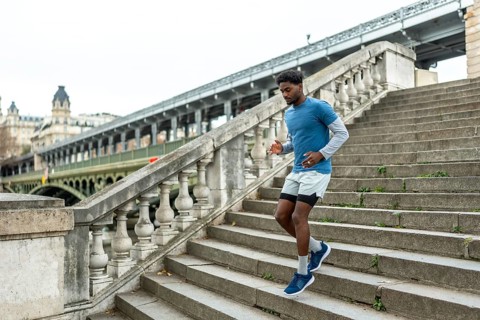 Young black man performing urban jogging and fitness training, actively descending large stone