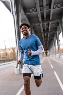 Smiling black man jogging on pariss bir hakeim bridge, staying fit and active in casual sportswear